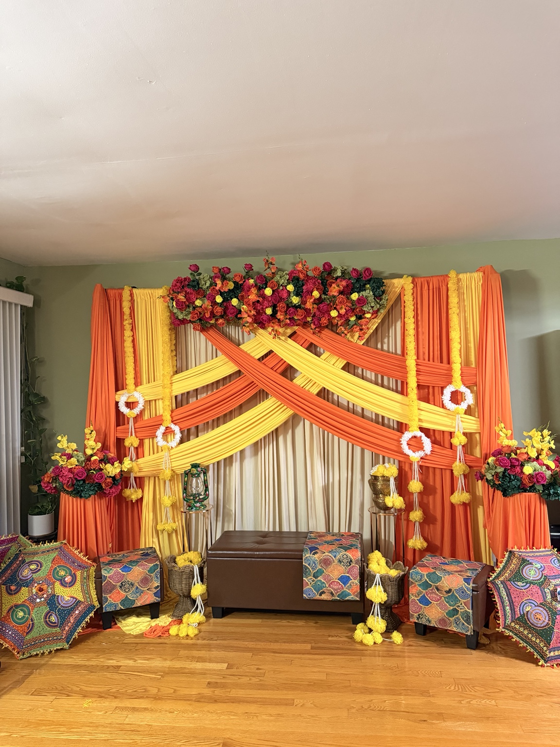 Orange and yellow Gaye Holud décor with floral wall, marigolds and colorful umbrellas by Arinay Events