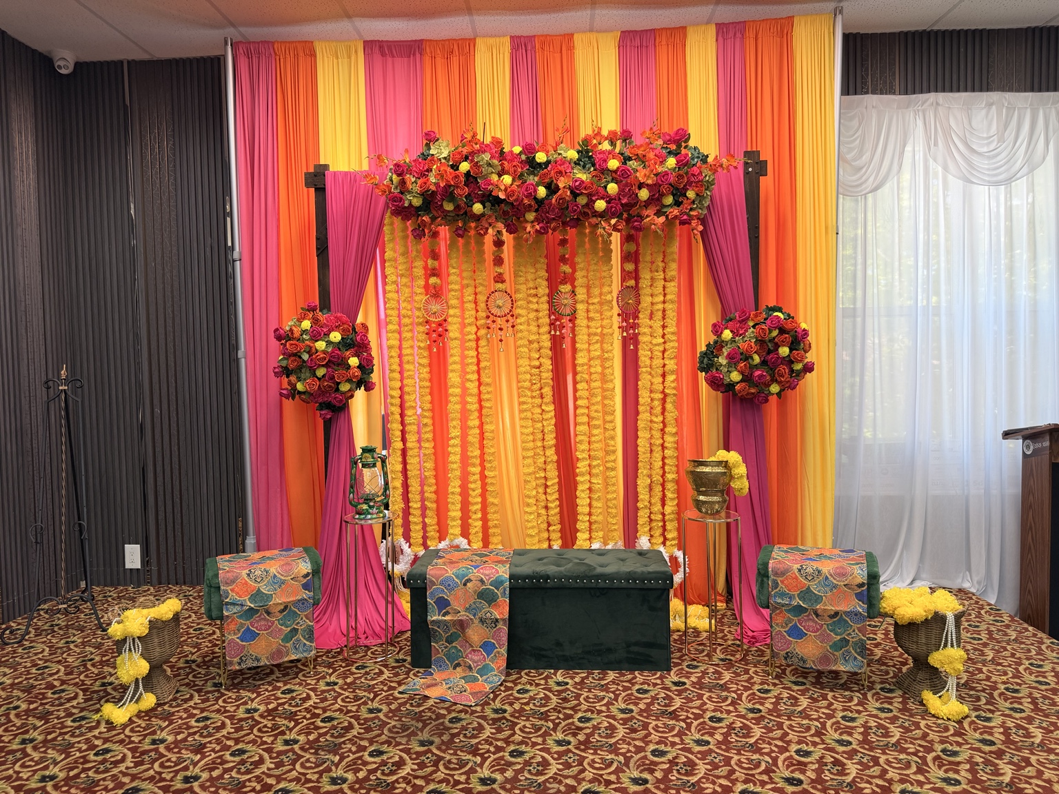 Bright orange, yellow and pink Gaye Holud stage with marigold garlands and floral arrangements by Arinay Events