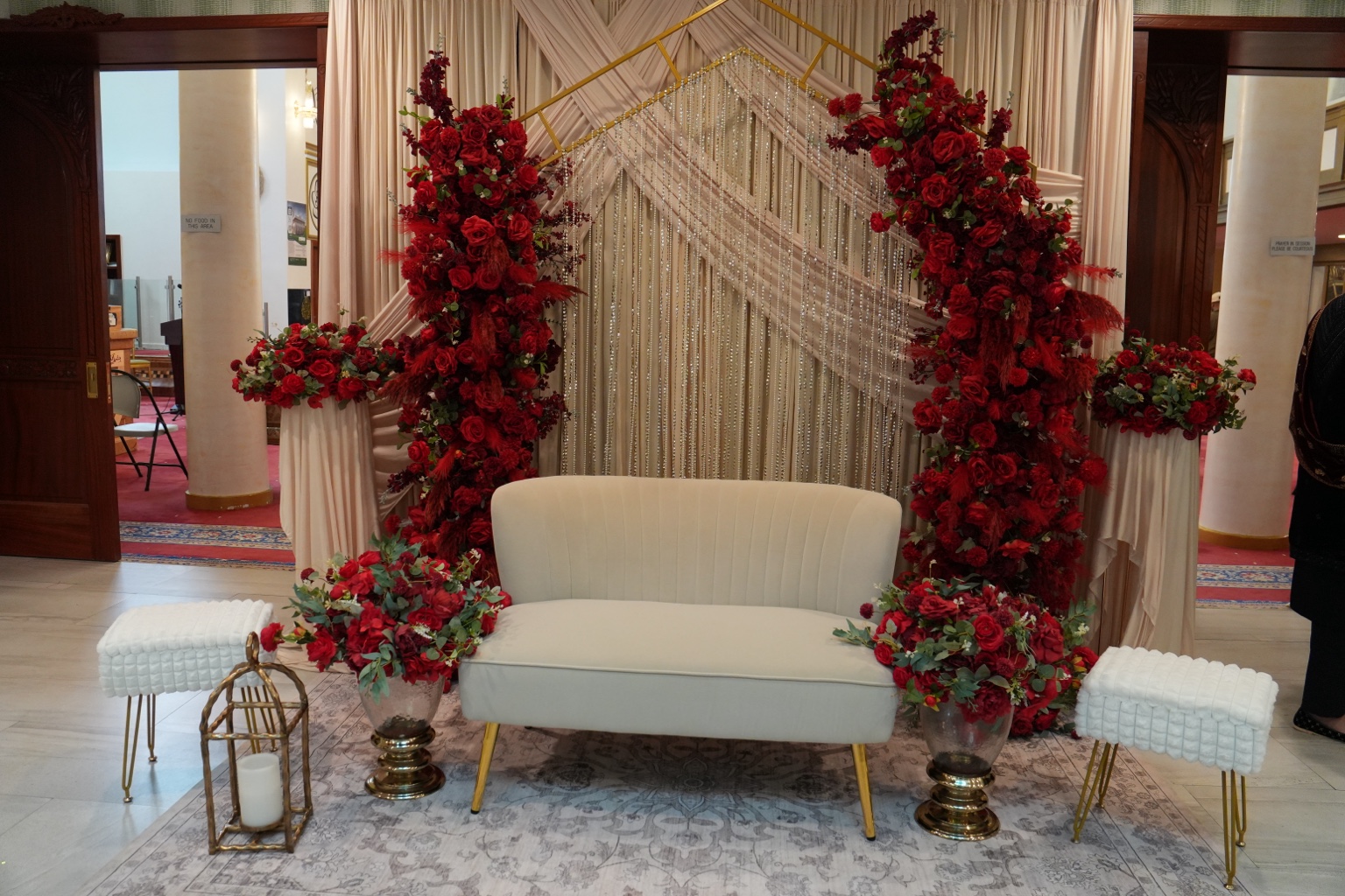 Wedding stage with dramatic red floral installations, ivory draping and gold accents by Arinay Events
